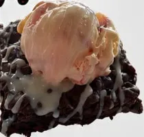 Brownie con una bola de helado y sirope blanco.