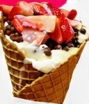 Cono de galleta relleno de crema con fresas y chispas de chocolate.